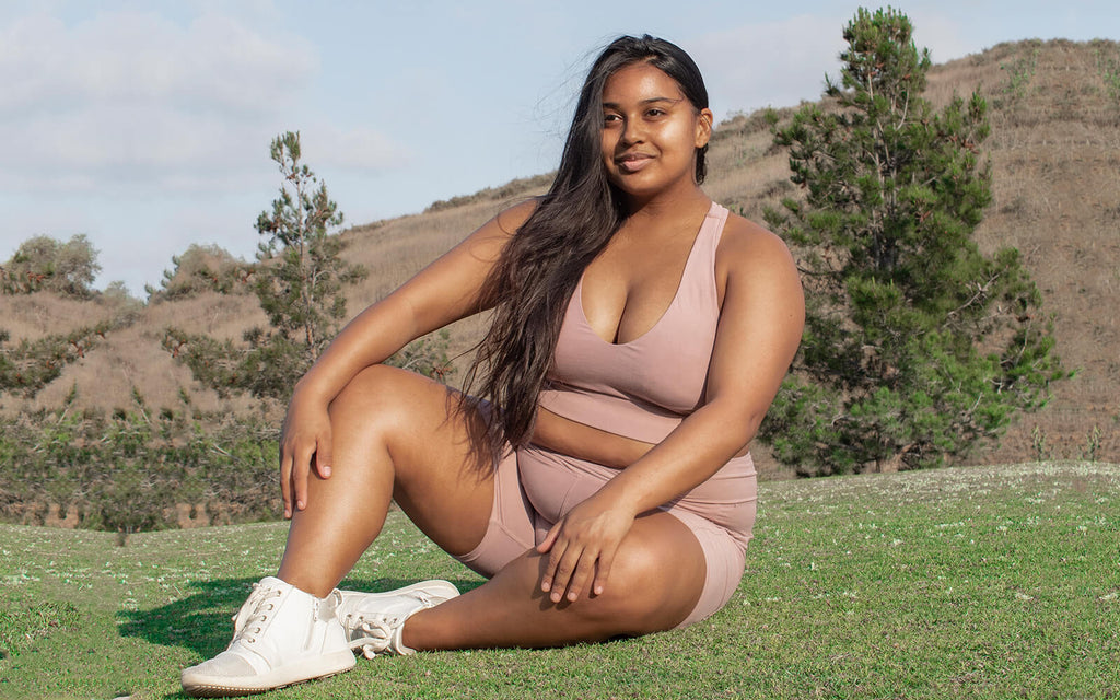 Wolven Wolf of the Month Ambassador Donchelle is wearing sustainable activewear made of recycled watter bottles in the color Salt. She has on bike shorts and a racerback bra and sits on grass