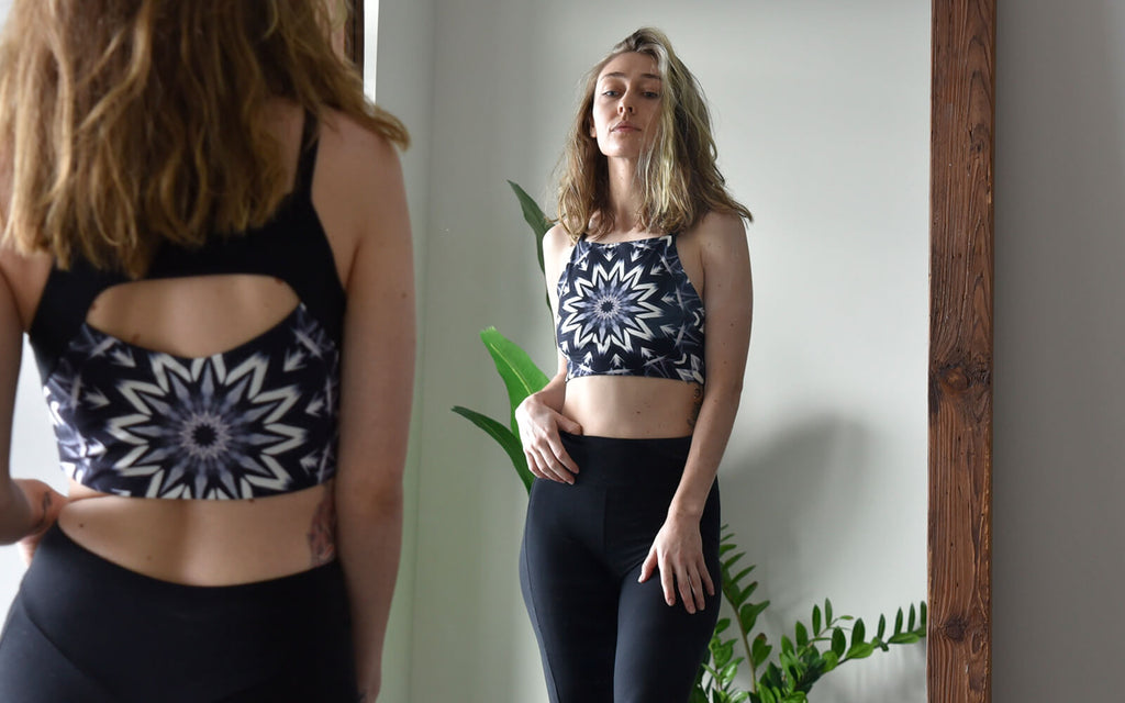 Wolf of the Month, Trish is staying in front of a mirror with one hand on her hip wearing sustainable activewear/yoga wear — Raina Reversible Four Way Top and Onyx Bell Bottoms