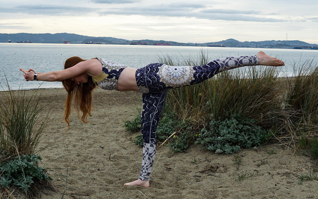 Wolf of the Month Danielle Dodson is wearing Wolven Threads sustainable activewear in Reverie print doing a yoga pose standing on the sand on a beach